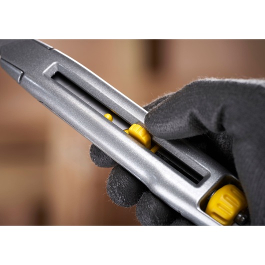 STANLEY 0-10-018 utility knife close-up, showing yellow slider and gloved hand holding the tool.