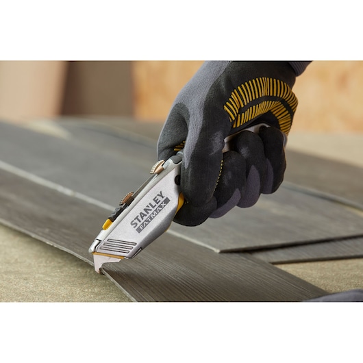 Stanley 0-10-789 utility knife held in gloved hand cutting dark laminate flooring.