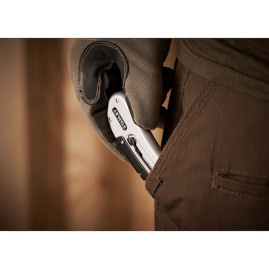 STANLEY 0-10-810 folding utility knife held by gloved hand, being placed in brown pants pocket, close-up.
