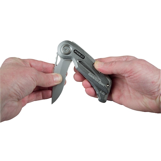 Photo of STANLEY 0-10-813 folding utility knife being opened with two hands, silver finish.