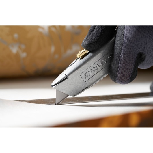 Photo of STANLEY 0-11-911 utility knife cutting paper held by a gloved hand.