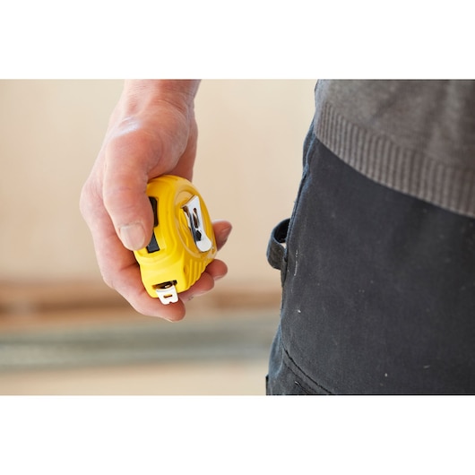 Photo of person holding STANLEY 0-30-497 yellow tape measure near work pants.