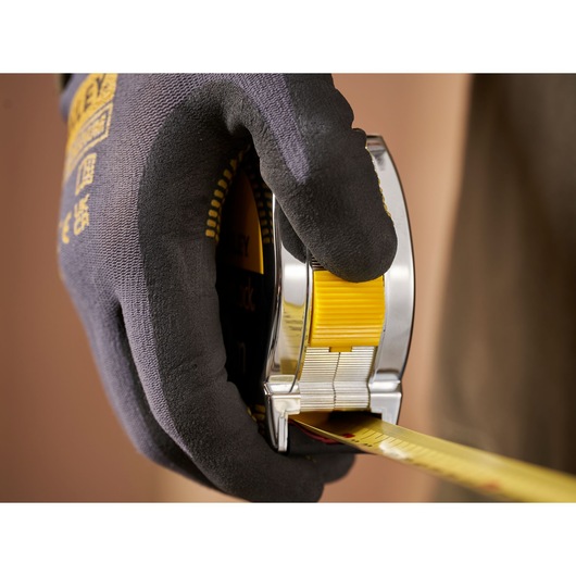 Close-up photo of STANLEY 0-33-442 tape measure held in gloved hand, showing yellow tape being extended.