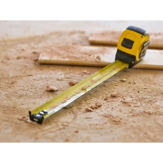 STANLEY 0-33-728 tape measure on a dusty workshop floor, extended and surrounded by wood and debris.