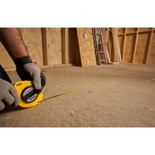 Stanley 0-34-105 measuring tape photography, yellow casing, extended on floor in construction setting.