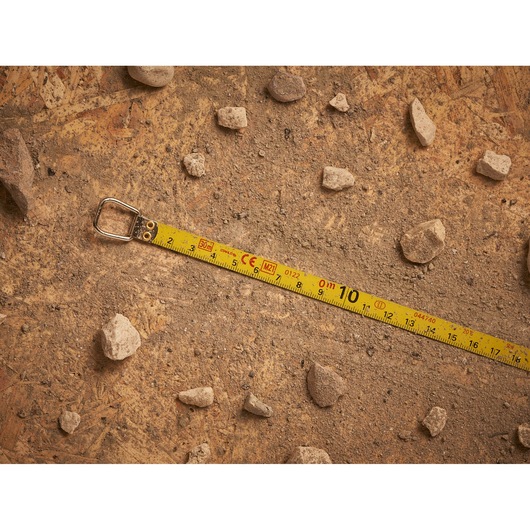 STANLEY 0-34-108 measuring tape extended on dirt with rocks, product photography.