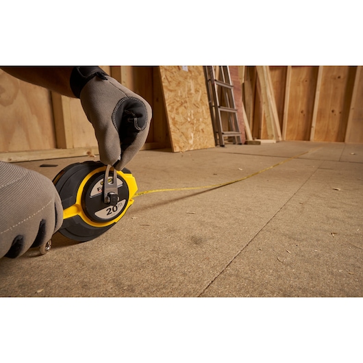 Photo of STANLEY 0-34-133 measuring tape reel in use on a construction floor, yellow tape extended.