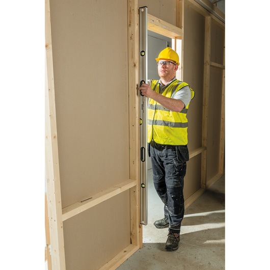 STANLEY 0-43-672 spirit level used vertically by worker in yellow vest at doorway, photography product.