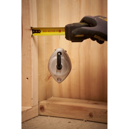 STANLEY 0-47-100 chalk line tool in use, hanging vertically with a hand measuring distance, construction setting.