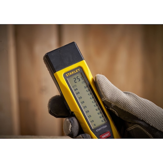 STANLEY 0-77-030 moisture meter held in gloved hand, showing digital display, close-up photography.