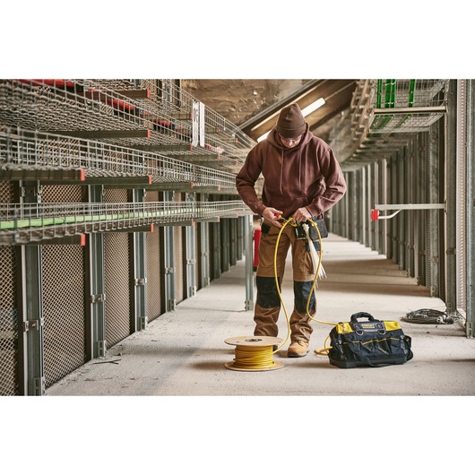 STANLEY 0-84-004 tool bag in yellow and black on floor near worker handling yellow cable spool in industrial setting.