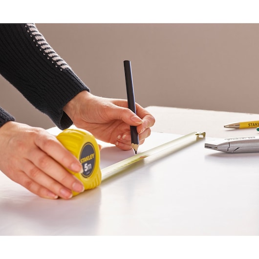 Photo of STANLEY 1-30-497 tape measure being used to mark a measurement on a white surface, with pencil and cutter visible.