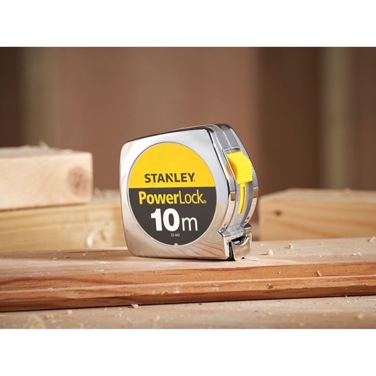 STANLEY 1-33-442 PowerLock 10m tape measure with yellow button on wood surface, side angle.