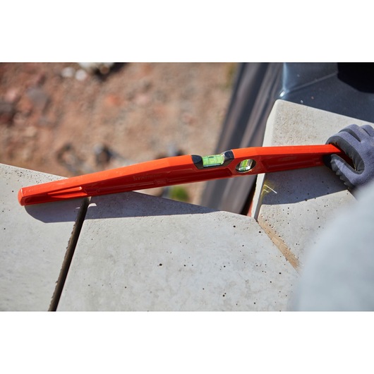 STANLEY 1-42-314 red spirit level in use on concrete tiles, close-up outdoor scene, product photography.