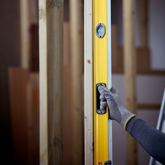 STANLEY 1-43-572 spirit level in use, yellow body with hand in work glove holding handle, construction background.
