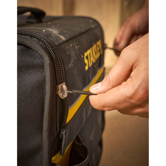 STANLEY 1-97-515 tool bag photography, close-up of hand using zipper on black and yellow fabric bag.