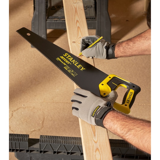 STANLEY 2-20-151 hand saw with yellow and black handle cutting a wooden plank, worker wearing gloves.
