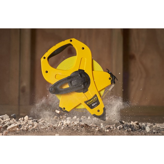 STANLEY 2-34-775 open reel yellow measuring tape, 60m length, handheld with black handle, on construction debris.