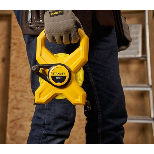 Photo of STANLEY 2-34-792 yellow 30m open reel tape measure held by a worker in gloves, construction setting.