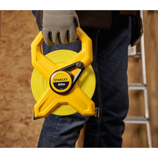 STANLEY 2-34-795 measuring tape 60m held by person wearing gloves, close-up, indoor work setting.