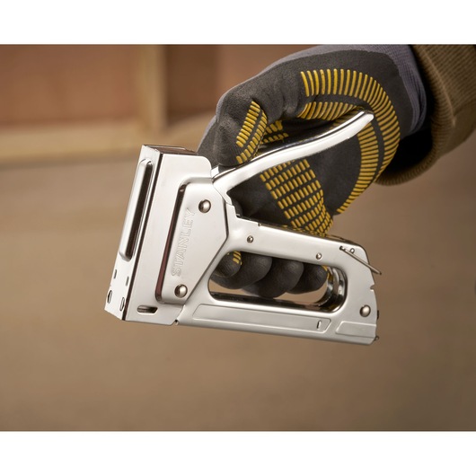 Photo of STANLEY 6-TR45 metal staple gun held by a gloved hand, close-up side view.