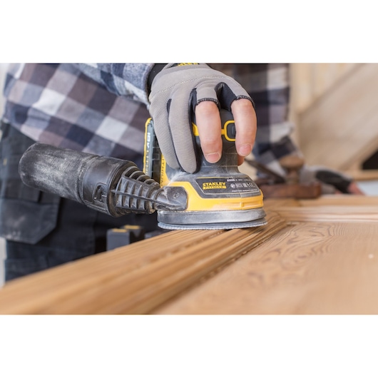 Photo of STANLEY FMCW220B sander in use on wood, close-up angle showing gloved hand holding tool.
