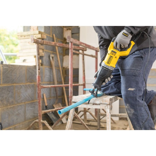 STANLEY FME360 reciprocating saw in use cutting a blue pipe at a construction site, angled side view.