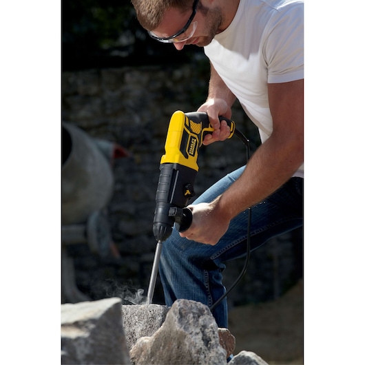 Photo of STANLEY FME500K corded rotary hammer drilling into stone, handheld during outdoor construction.