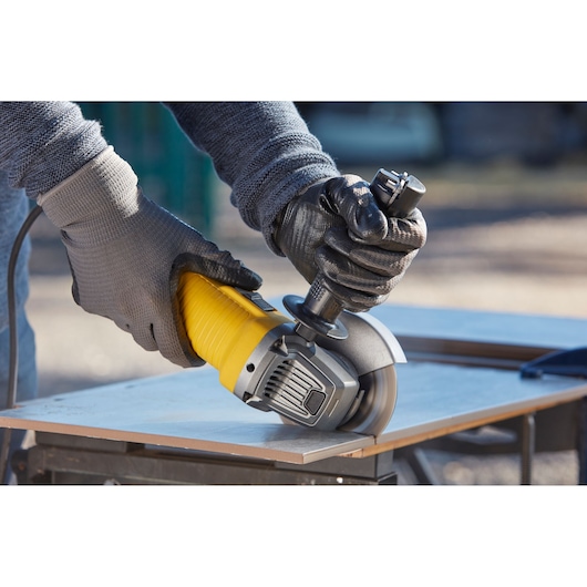 STANLEY FMEG220 angle grinder in use, gloved hands cutting a tile outdoors.