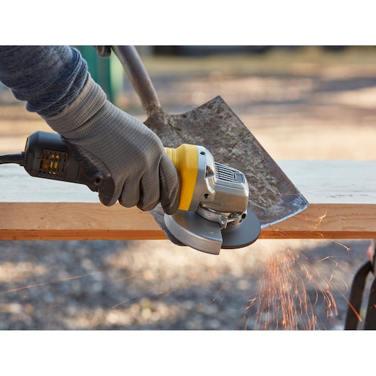 Photo of STANLEY FMEG220 angle grinder in use, grinding a shovel blade, sparks visible.