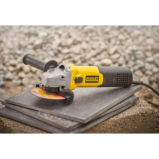 STANLEY FMEG225VS angle grinder with yellow and black handle on stone tiles, side view.