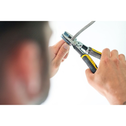 Stanley FMHT0-75469 pliers with yellow and black grips held by hands cutting a cable in close-up.