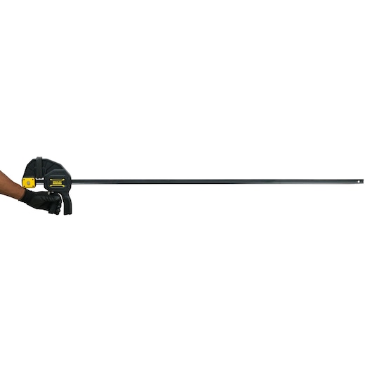 Stanley FMHT0-83242 bar clamp in black and yellow, side angle, held by gloved hand, white background.