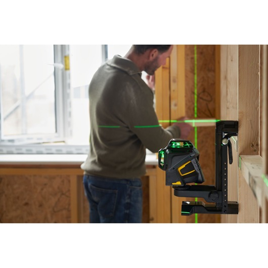 STANLEY FMHT1-77356 cross line laser level mounted on bracket projecting green lines in a wooden construction setting.