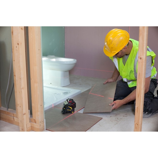 STANLEY FMHT1-77357 laser level used by worker aligning floor tiles in bathroom under construction.
