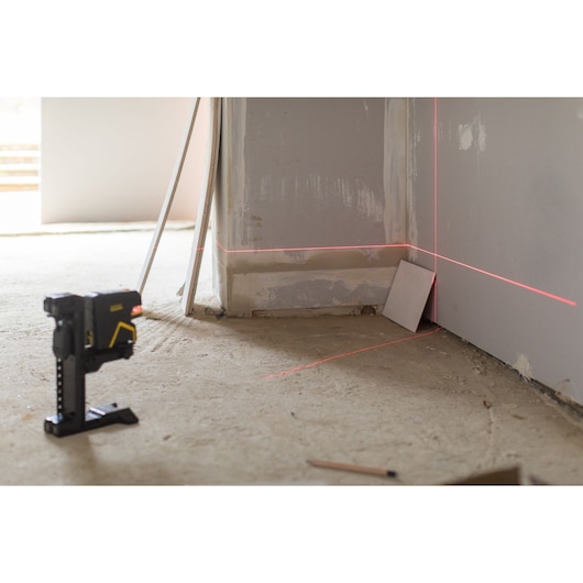 STANLEY FMHT1-77415 laser level projecting red lines on walls in construction setting, side angle.