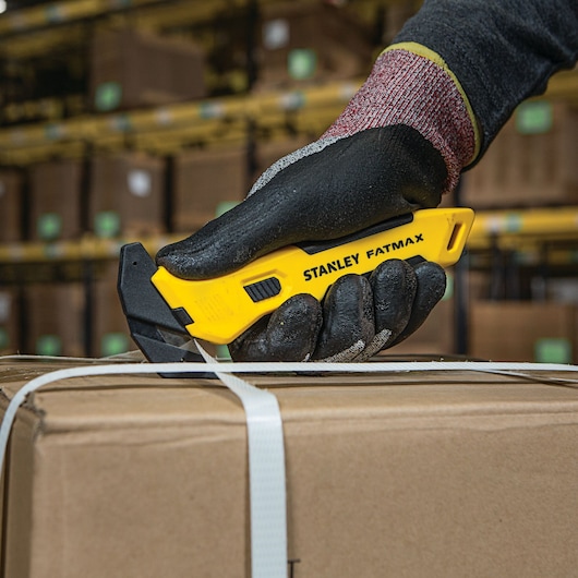 STANLEY FMHT10358 utility knife cutting packing strap on cardboard box, close-up view in warehouse.