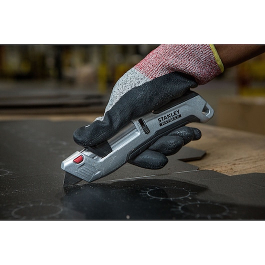 Photo of STANLEY FMHT10367-0 utility knife in gloved hand cutting black material.