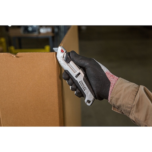 Stanley FMHT10367-0 utility knife cutting cardboard, held in gloved hand, product in use.