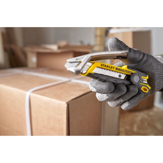 STANLEY FMHT10592-0 utility knife held in gloved hand, cutting box strap in a warehouse setting.
