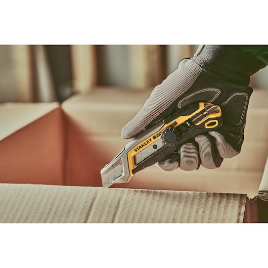 Stanley FMHT10592-0 utility knife cutting cardboard, shown in gloved hand, product photography.