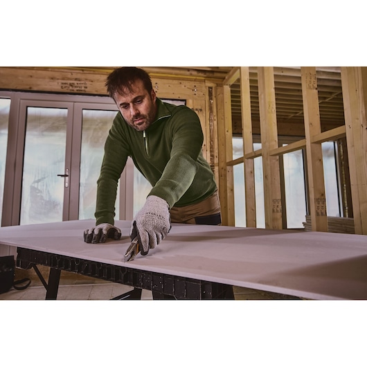 Stanley FMHT10592-0 utility knife used to cut drywall on a workbench in a construction interior.
