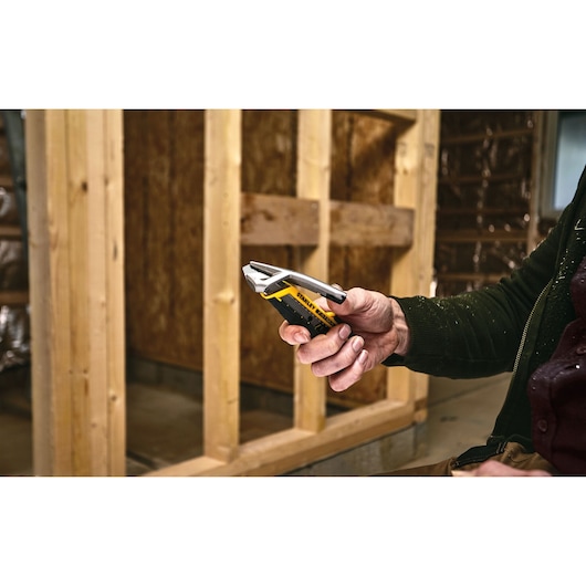 STANLEY FMHT10594-0 utility knife held in hand at construction site, yellow and black handle visible.