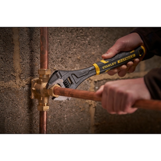 Photo of STANLEY FMHT13127-0 adjustable wrench used on copper pipe, product held by hand near wall.