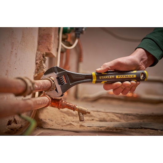 Photo of STANLEY FMHT13128-0 adjustable wrench turning a pipe fitting, close-up in a plumbing setting.
