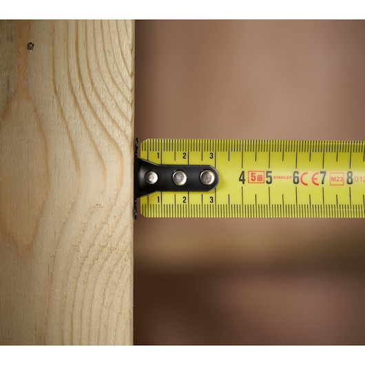 STANLEY FMHT31725-0 tape measure close-up measuring a wooden plank, yellow tape with black markings.