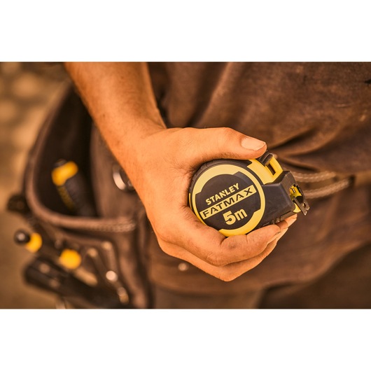 Photo of STANLEY FMHT33100-0 FATMAX 5m tape measure held in hand, tool belt in background.