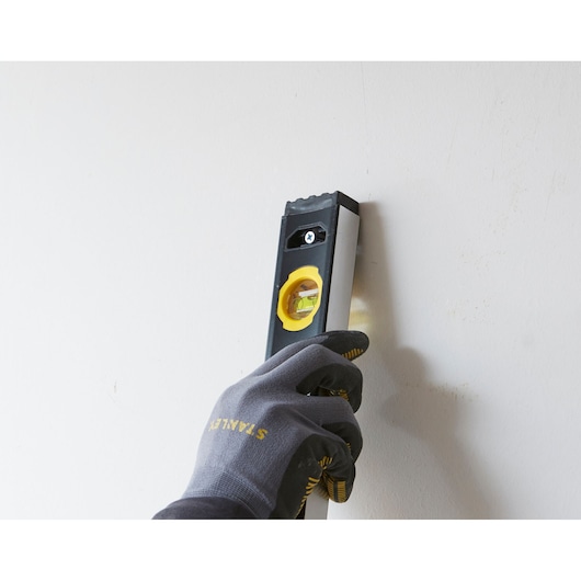 STANLEY FMHT42554-1 spirit level held vertically against a wall by a gloved hand.