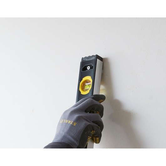 STANLEY FMHT42559-1 spirit level held vertically against a wall by a gloved hand, side angle.