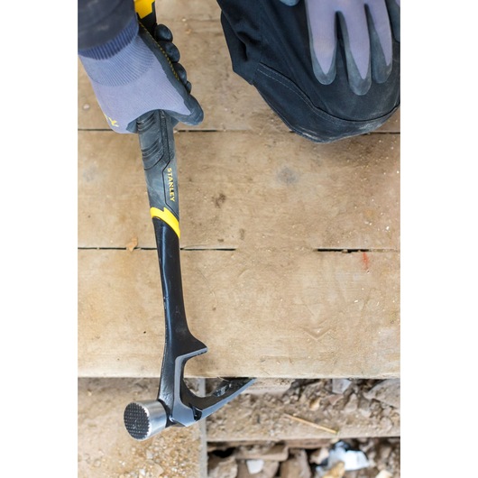Photo of STANLEY FMHT51367-2 claw hammer in use on wood floor, black and yellow handle, shown with gloved hand.